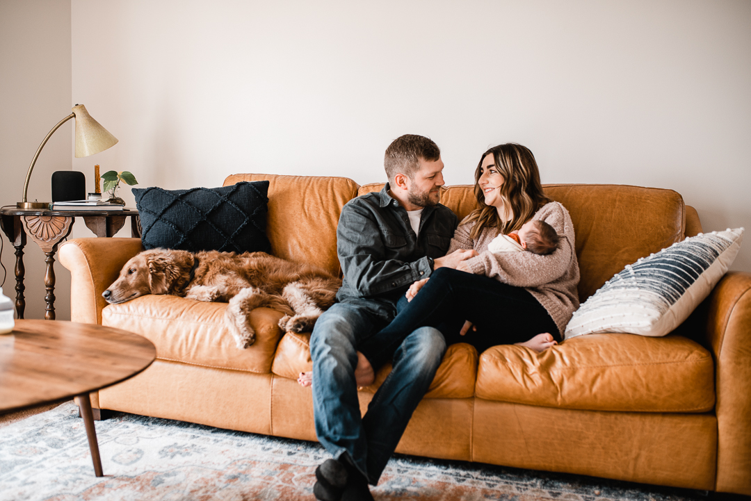 Family cuddles on the couch with their dog in Omaha during their lifestyle newborn photo session with Melissa Lindquist Photography.